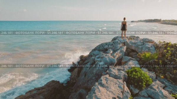 Traveler gazes over turquoise ocean from rocky cliff during golden hour in Tulum Mexico. Стоковое видео, видеограф Ольга Сухарева / Фотобанк Лори