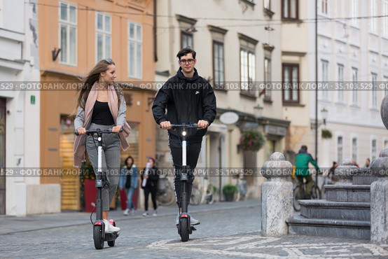 Trendy fashinable teenagers riding public rental electric scooters in urban city environment. New eco-friendly modern public city transport in Ljubljana, Slovenia. Стоковое фото, фотограф Matej Kastelic / Фотобанк Лори