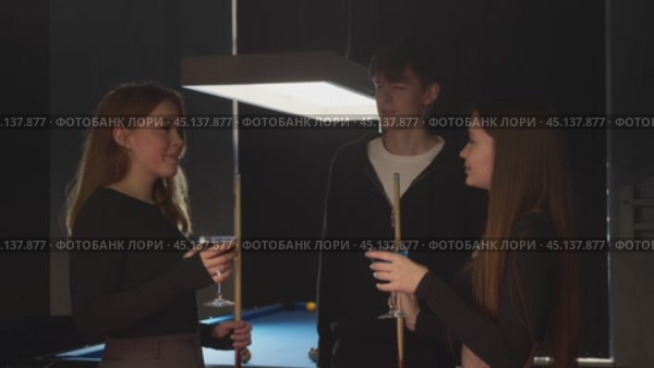 Two beautiful girls and a young man relax in between playing billiards drinking alcoholic cocktails at the bar. Стоковое видео, видеограф Strunov David / Фотобанк Лори