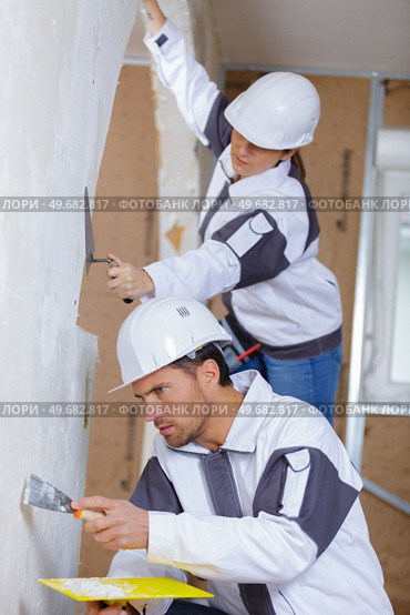 two builders in hardhats and overalls with spatula repairing room. Стоковое фото, агентство Ingram Publishing / Фотобанк Лори