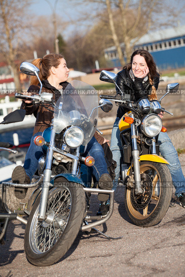 Two Caucasian women motorcyclists talk incessantly while sitting face-to-face on their motorcycles, spring season. Стоковое фото, фотограф Кекяляйнен Андрей / Фотобанк Лори