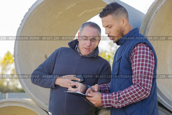 two coworkers discussing in cement pipes yard. Стоковое фото, агентство Ingram Publishing / Фотобанк Лори
