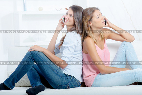 two girls with smartphones sitting on sofa at home. Стоковое фото, агентство Ingram Publishing / Фотобанк Лори