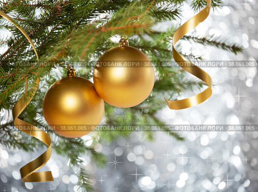 Two gold baubles and serpentine curls on a branch of a christmas tree, on a silver bokeh background with sparkles. Стоковое фото, фотограф Юлия Бабкина / Фотобанк Лори