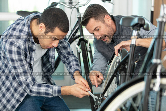 two guys examine bicycle in sport workshop. Стоковое фото, агентство Ingram Publishing / Фотобанк Лори