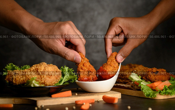 Two hand holding crispy fried chicken dipped in tomato sauce.Selective focus. Стоковое фото, агентство Ingram Publishing / Фотобанк Лори