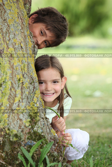 Two little children hiding behind tree. Стоковое фото, агентство Ingram Publishing / Фотобанк Лори