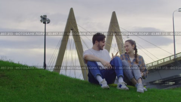 Two lovers kissing in the park on the grass against the backdrop of the urban landscape. Стоковое видео, видеограф Strunov David / Фотобанк Лори