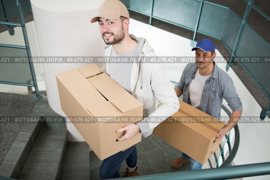 two male movers walking upward with boxes on staircase. Стоковое фото, агентство Ingram Publishing / Фотобанк Лори