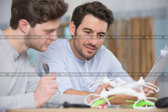 two men following instructions to assemble a drone. Стоковое фото, агентство Ingram Publishing / Фотобанк Лори