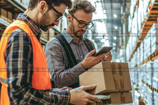 Two men in orange vests are looking at a box on a pallet. Стоковое AI-изображение, AI-художник Ярославский Максим / Фотобанк Лори