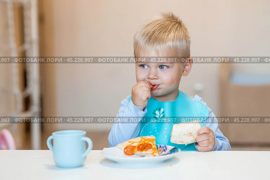 Unhealthy food for children. Eating. A cute 2-year-old kid eats pizza for lunch. Fast food. Family and children. Стоковое фото, фотограф Photojuli / Фотобанк Лори
