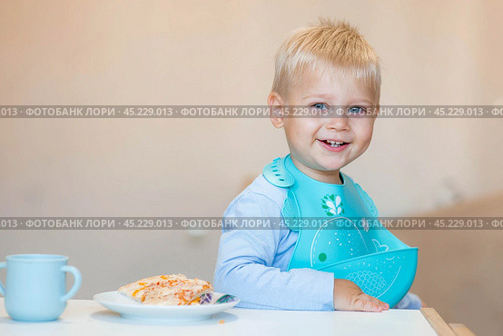 Unhealthy food for children. Eating. A cute 2-year-old kid eats pizza for lunch. Fast food. Family and children. Стоковое фото, фотограф Photojuli / Фотобанк Лори