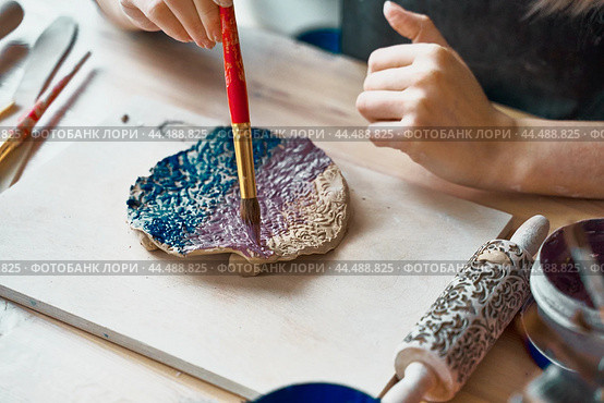 Unrecognised Woman making pattern on ceramic plate, hands close-up, focus on palms with paint brush. Creative hobby concept. Earn extra money, side hustle, turning hobbies into cash, passion into job. Стоковое фото, фотограф Natalia Gdovskaia / Фотобанк Лори