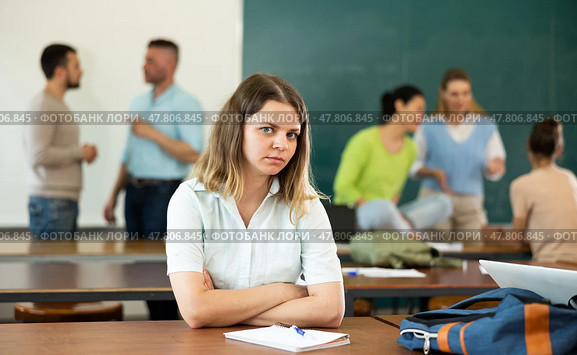 Upset girl sitting at table in auditorium during break on background with students. Стоковое фото, фотограф Яков Филимонов / Фотобанк Лори
