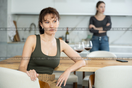 Upset middle-aged woman sitting at the kitchen table with her back to another lady quarreling to her. Стоковое фото, фотограф Яков Филимонов / Фотобанк Лори