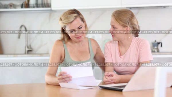Upset teenage girl reading letter about exam results while sitting at home table with concerned mother offering comfort and understanding to daughter. Стоковое видео, видеограф Яков Филимонов / Фотобанк Лори