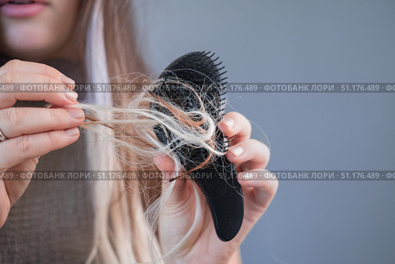 Upset young woman holding hairbrush with many fallen strands showing early signs of hair loss and breakage. Стоковое фото, фотограф Svetlana Golovco / Фотобанк Лори