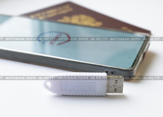 Устройство  USB eToken  (рутокен) белого цвета, устройство для хранения электронной цифровой подписи (ЭЦП) и информации для аутентификации пользователя, паспорт и телефон с приложением Госуслуги на белом фоне. Редакционное фото, фотограф Snezka / Фотобанк Лори