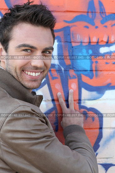 V for Victory from a man in front of grafitti. Стоковое фото, агентство Ingram Publishing / Фотобанк Лори