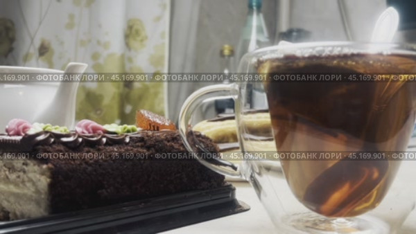 В прозрачную чашку наливают кипяток из чайника и заваривают чай. На столе лежат пирожные и тортик. Стоковое видео, видеограф Ярославский Максим / Фотобанк Лори