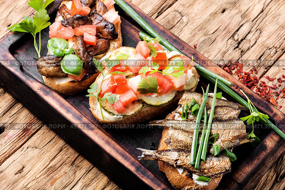 Variety of small sandwiches.Bruschetta on wooden cutting board.Bruschetta is traditional Italian common folk dish.. Bruschetta with various toppings. Стоковое фото, агентство Ingram Publishing / Фотобанк Лори