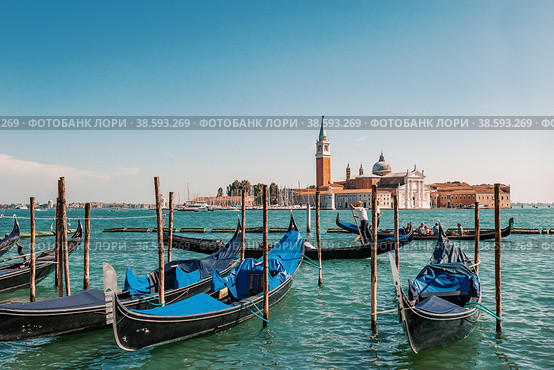 VENICE, ITALY-SEPTEMBER 4, 2018 Venetian gondolier punting gondola through grand canal waters - View of San Giorgio Island in Venice with wooden buoys in Giudecca Canal. Редакционное фото, фотограф Оксана Медведева / Фотобанк Лори