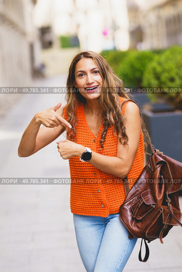 Vertical photo of a latin woman complaining about time pointing her wrist watch outdoors. Woman complaining about time pointing her wrist watch outdoors. Стоковое фото, агентство Ingram Publishing / Фотобанк Лори