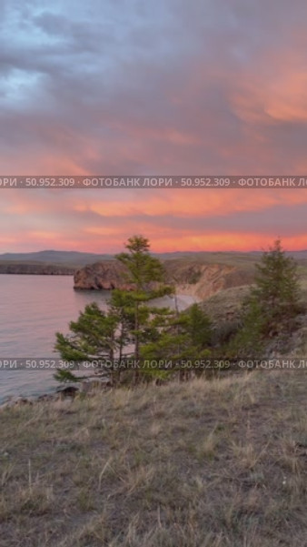 Vertical video of summer evening on Lake Baikal. Panoramic view of Olkhon Island coast and pink clouds at sunset. Natural background. Picturesque sunset landscape. Стоковое видео, видеограф Виктория Катьянова / Фотобанк Лори