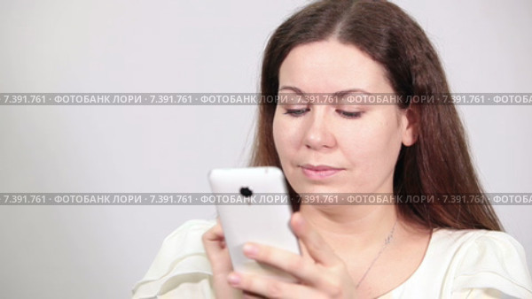 Веселая девушка листает страницы на экране телефона и пишет сообщения, серый фон. Стоковое видео, видеограф Кекяляйнен Андрей / Фотобанк Лори