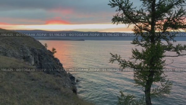 Video of Baikal Lake in evening. Silhouette of green larch trees on shore of Olkhon Island against the backdrop of colorful sunset sky. Picturesque landscape, natural background. Стоковое видео, видеограф Виктория Катьянова / Фотобанк Лори