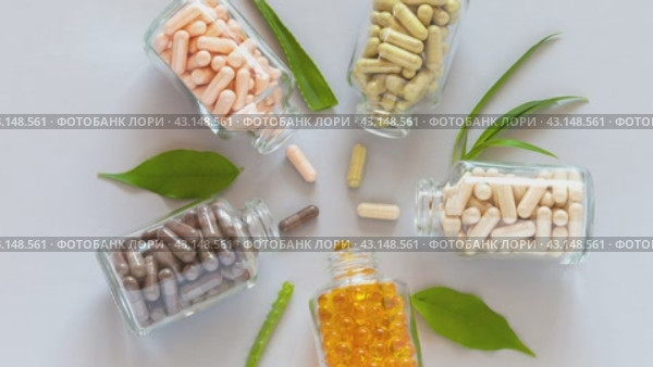 Video of glass vials with capsules of food bio additives and green plants on light background. Five types of natural dietary supplements with herbals and omegas. Flat lay, close-up, top view. Стоковое видео, видеограф Виктория Катьянова / Фотобанк Лори