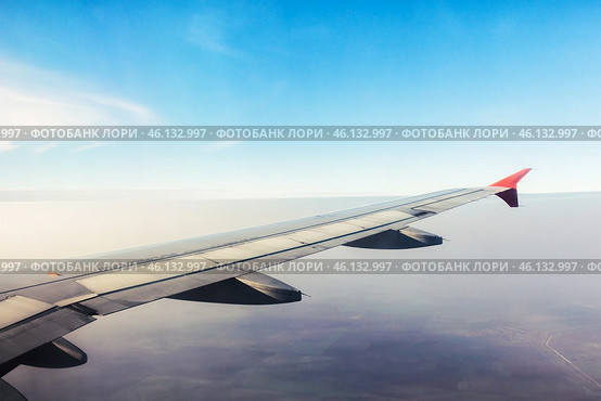 View of airplane wing against clear blue sky during daytime flight over tranquil landscape. Стоковое фото, фотограф Сергей Толмачёв / Фотобанк Лори