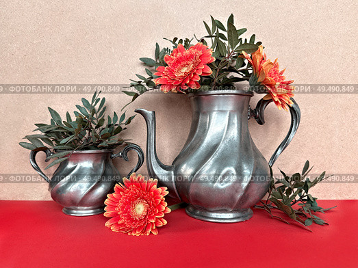 Vintage Pewter Teapots with Bright Orange Gerbera Flowers and Greenery on Red Surface. Стоковое фото, фотограф Аnna Ivanova / Фотобанк Лори