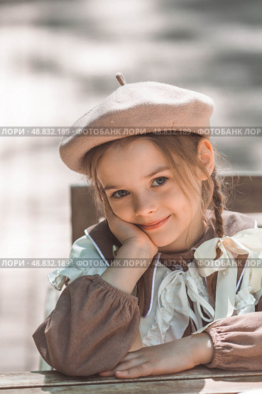 Vintage women's accessories and retro-style clothing. A small, beautiful girl with bows in her hair, in a beige dress and a beret outdoors. Стоковое фото, фотограф Photojuli / Фотобанк Лори
