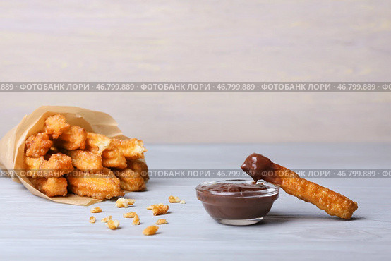Вкусные чуррос в пергаменте и соусе из расплавленного шоколада на светлом деревянном фоне. Стоковое фото, фотограф Pixel_shot / Фотобанк Лори