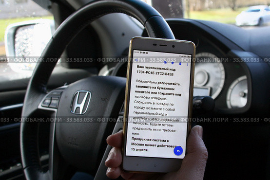 Водитель держит смартфон с полученным цифровым пропуском для передвижения по городу. Пандемия коронавируса COVID-19 в Москве (2020 год). Редакционное фото, фотограф Щеголева Ольга / Фотобанк Лори