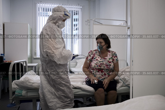 Врач в защитном костюме от COVID-19 снимает показания у пациента в инфекционном отделении в красной зоне медицинского центра ​помощи и спасения. Богучаны, Красноярский край, Россия (2021 год). Редакционное фото, фотограф Светлана Попова / Фотобанк Лори