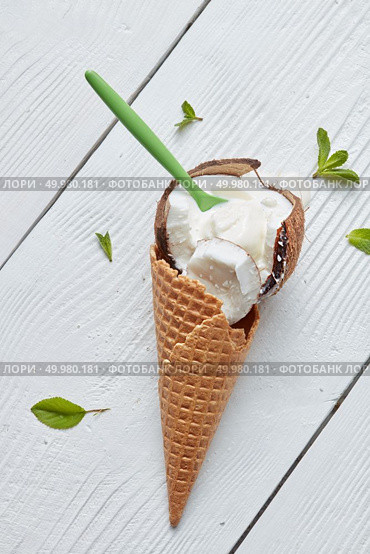 Waffle cone with ice cream in coconut with a spoon and mint leaves On white wooden background flat lay. Ice cream in waffle cone. Стоковое фото, агентство Ingram Publishing / Фотобанк Лори