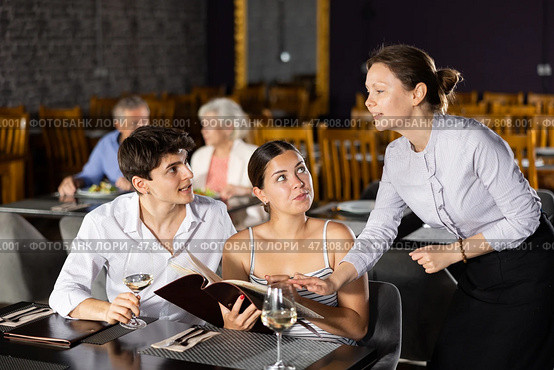 Waitress helps to sort out menu, choose original dish to young married couple. Стоковое фото, фотограф Яков Филимонов / Фотобанк Лори