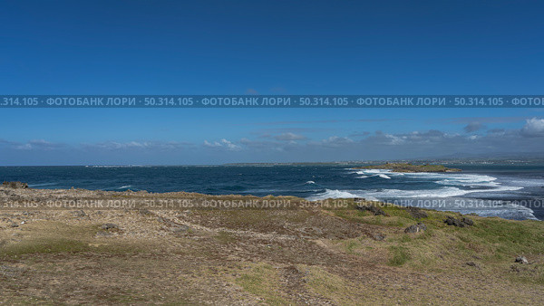 Waves are raging in the blue ocean in the strait between two islets. White foam on the surface of the water. Volcanic boulders, green grass on the shore of the island. Azure sky, clouds. Mauritius. (2024 год). Стоковое фото, фотограф Вера Ивановна Кубарева / Фотобанк Лори