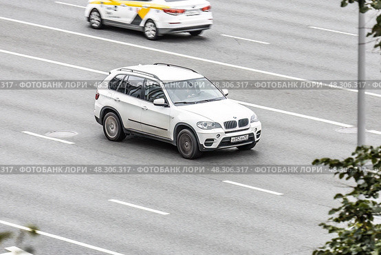 White BMW X5 car is moving on city street. Automobile driving fast along urban speedway with blurred background. Редакционное фото, фотограф Константин Григорьев / Фотобанк Лори