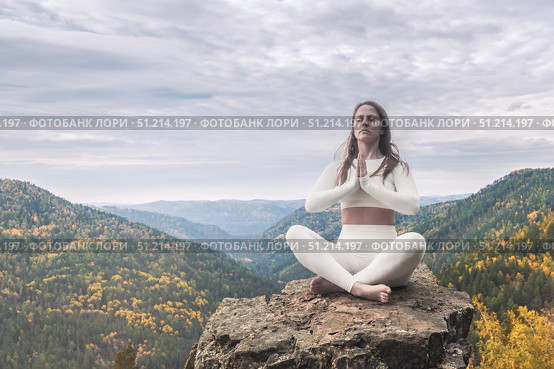 White woman practices yoga in lotus position while meditating on rocky cliff surrounded by autumn mountains. Yoga practice and outdoor fitness. Стоковое фото, фотограф Владимир Разгуляев / Фотобанк Лори