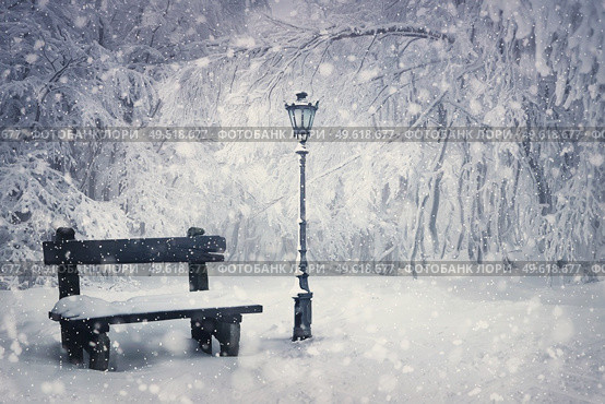 Winter time scene with a wooden bench and street lamp covered with snow under a snowfall in the park. Wonderful holiday season background, Merry Christmas magic atmosphere. Tranquil and peaceful view. Стоковое фото, агентство Ingram Publishing / Фотобанк Лори