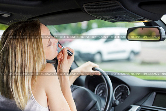 woman applys lipstick in front of rearview mirror in car. Стоковое фото, агентство Ingram Publishing / Фотобанк Лори