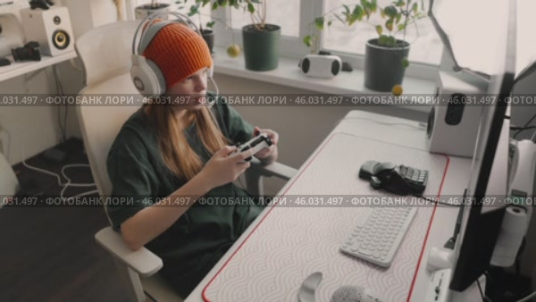 Woman balancing gaming and studies in stylish setup. Modern workspace with computer, monitor, headphones, microphone, and pc accessories emphasizes comfort, technology, and professional multitasking. Стоковое видео, видеограф Енваев Андрей / Фотобанк Лори