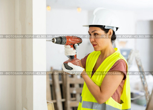 Woman builder using drill to bore hole in wall. Стоковое фото, фотограф Яков Филимонов / Фотобанк Лори