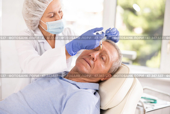 Woman cosmetologist making injections between eyebrows to male patient. Стоковое фото, фотограф Яков Филимонов / Фотобанк Лори