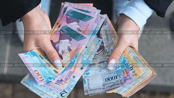 Woman displaying fanned venezuelan bolivar banknotes, highlighting financial exchange. Стоковое фото, фотограф Mikhail Davidovich / Фотобанк Лори