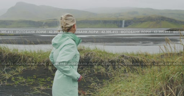 Woman enjoying outdoor Iceland Seljalandsfoss waterfall from far distance. Стоковое видео, видеограф Igor Tichonow / Фотобанк Лори